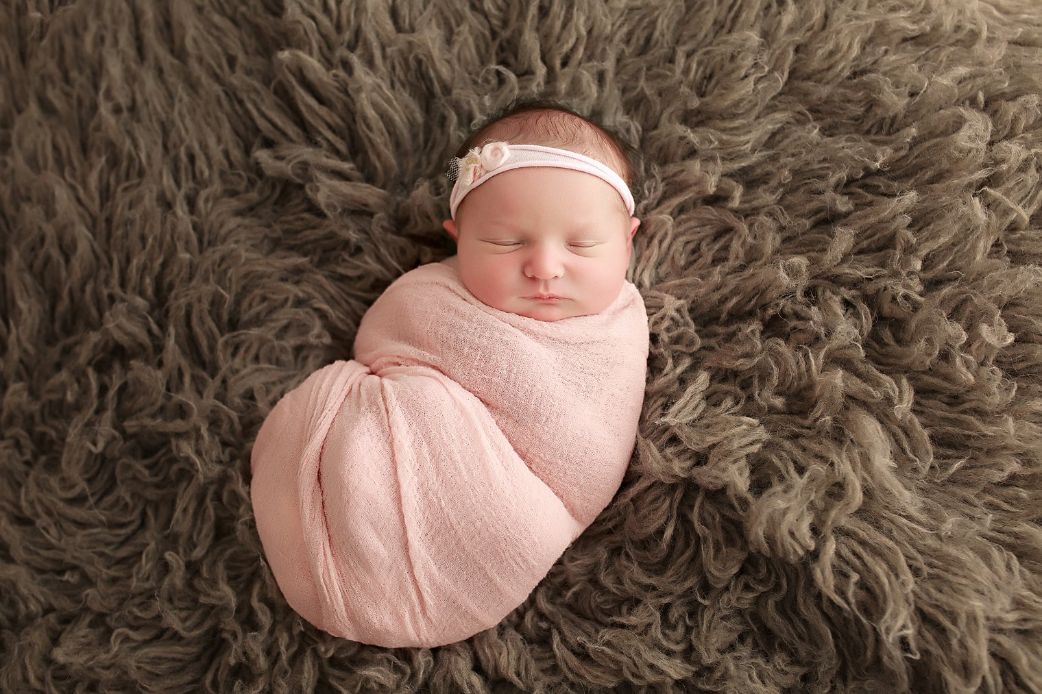 newborn baby girl in pink on gray flokati fur