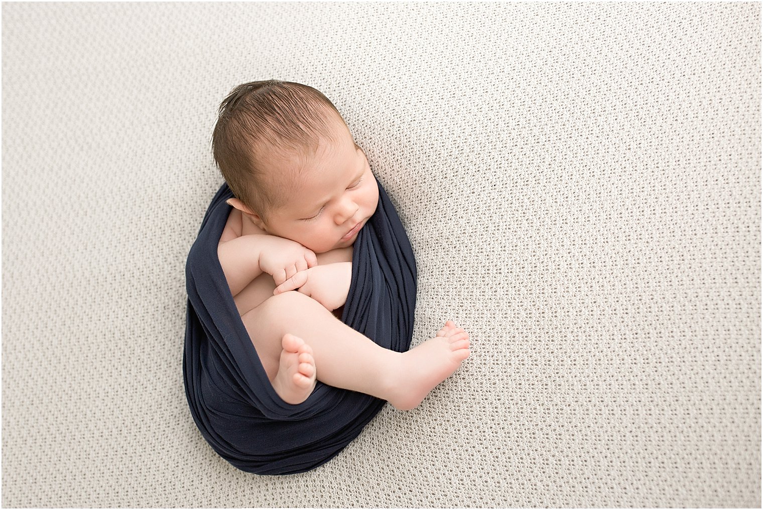 Newborn boy on white blanket and navy wrap