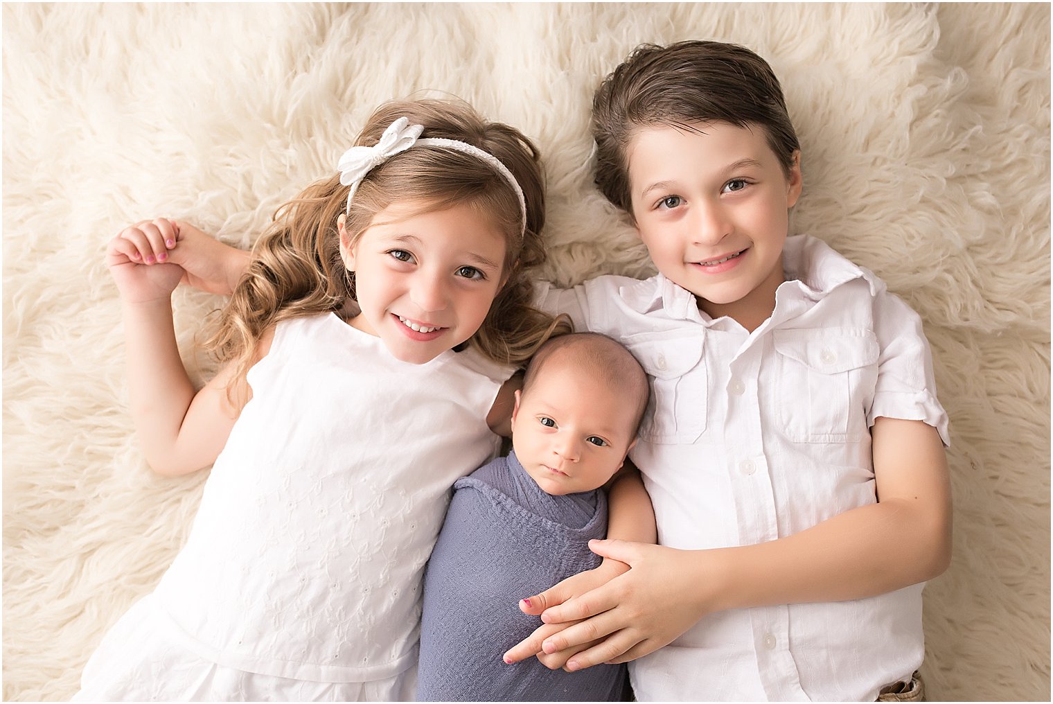 Studio session of older siblings with newborn brother