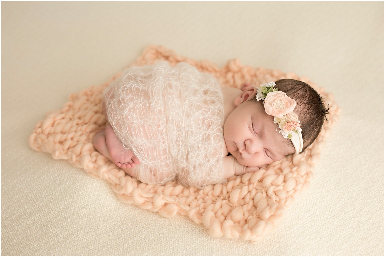 Sleepy newborn girl in peach and cream