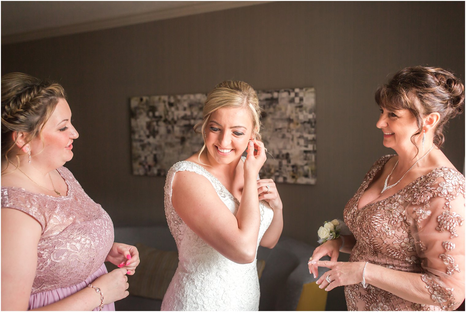 Bride putting on earrings with mom and maid of honor