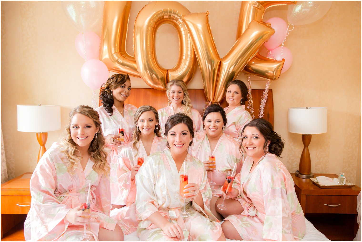 Photo of bride and bridesmaids on bed drinking mimosas