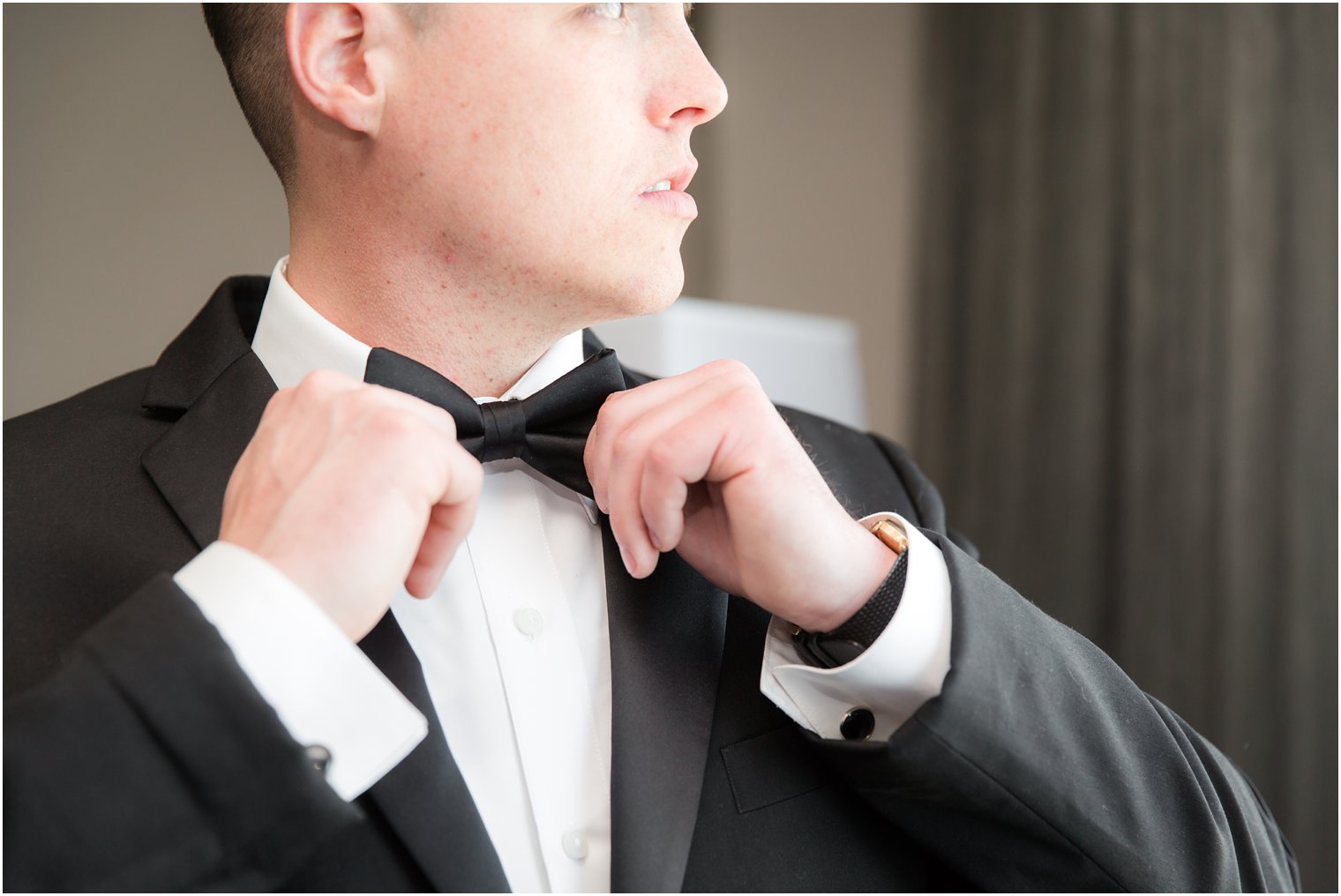 groom putting on bow tie for black tie wedding