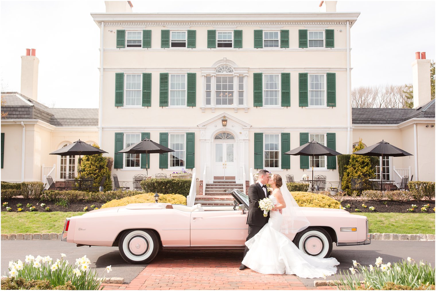 bride and groom posing in front of convertible pink Cadillac