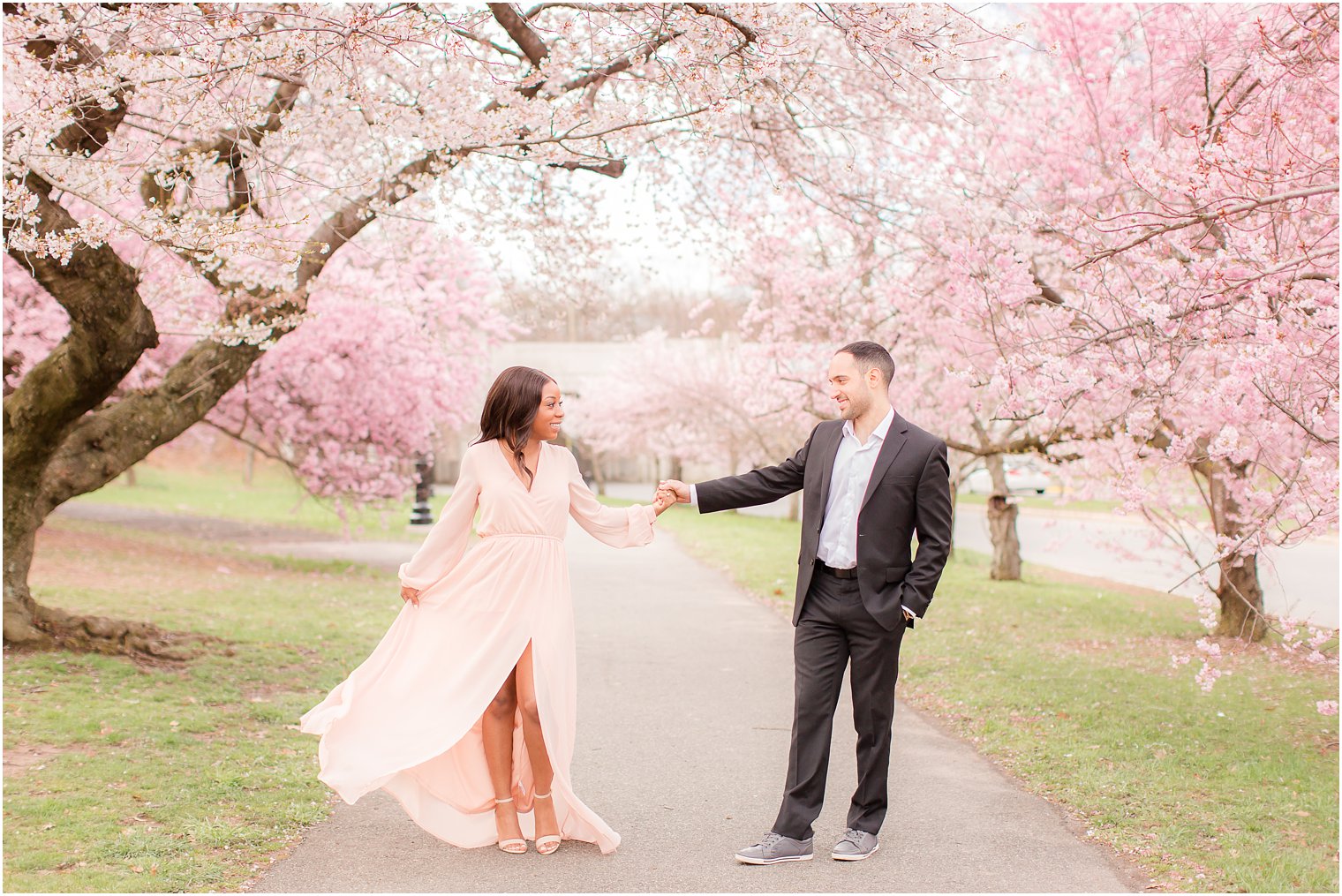 groom twirling his bride during engagement photos with cherry blossoms