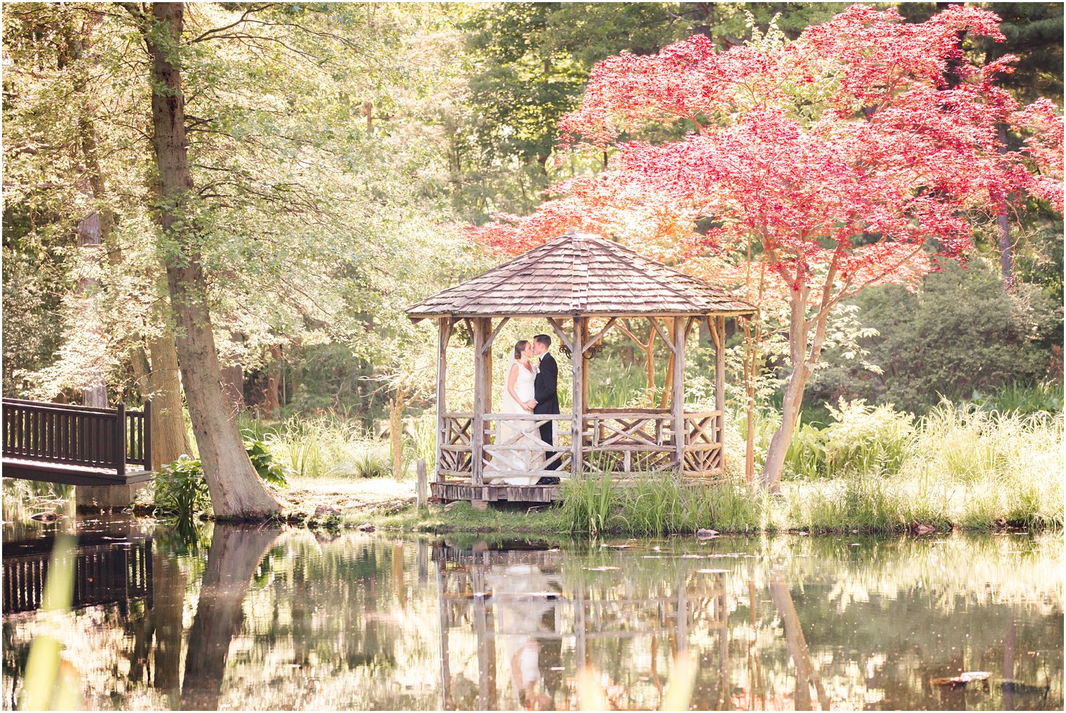 romantic portrait of bride and groom in a gazebo in front of a reflective pond