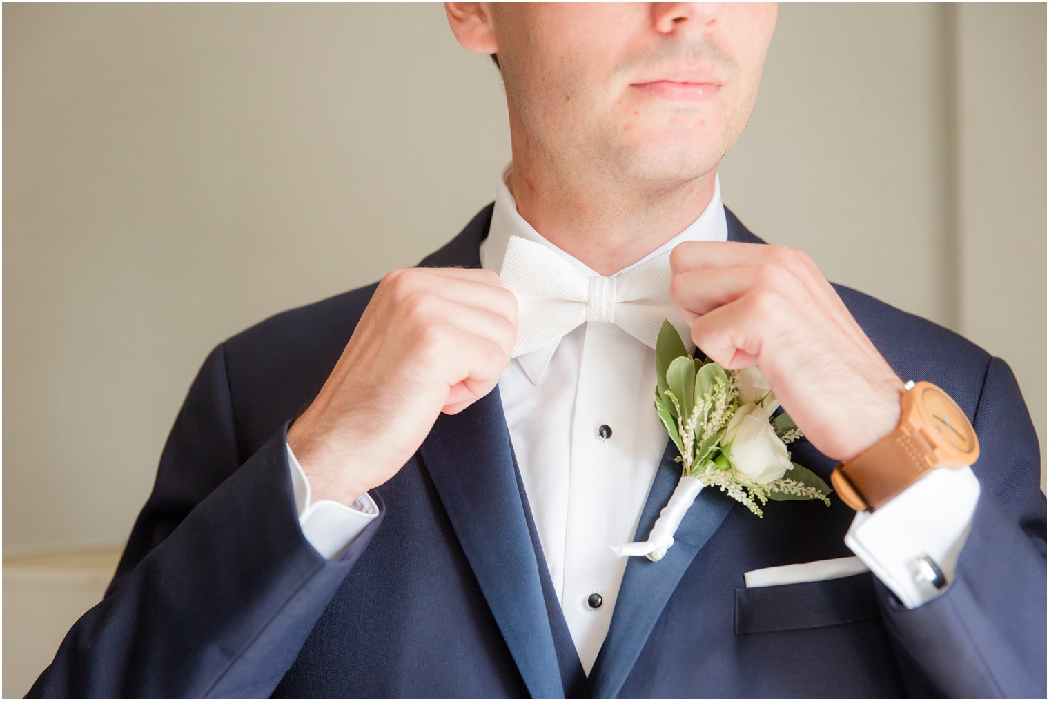 Groom wearing navy blue suit jacket adjusts white tie for classic Park Savoy Estate wedding