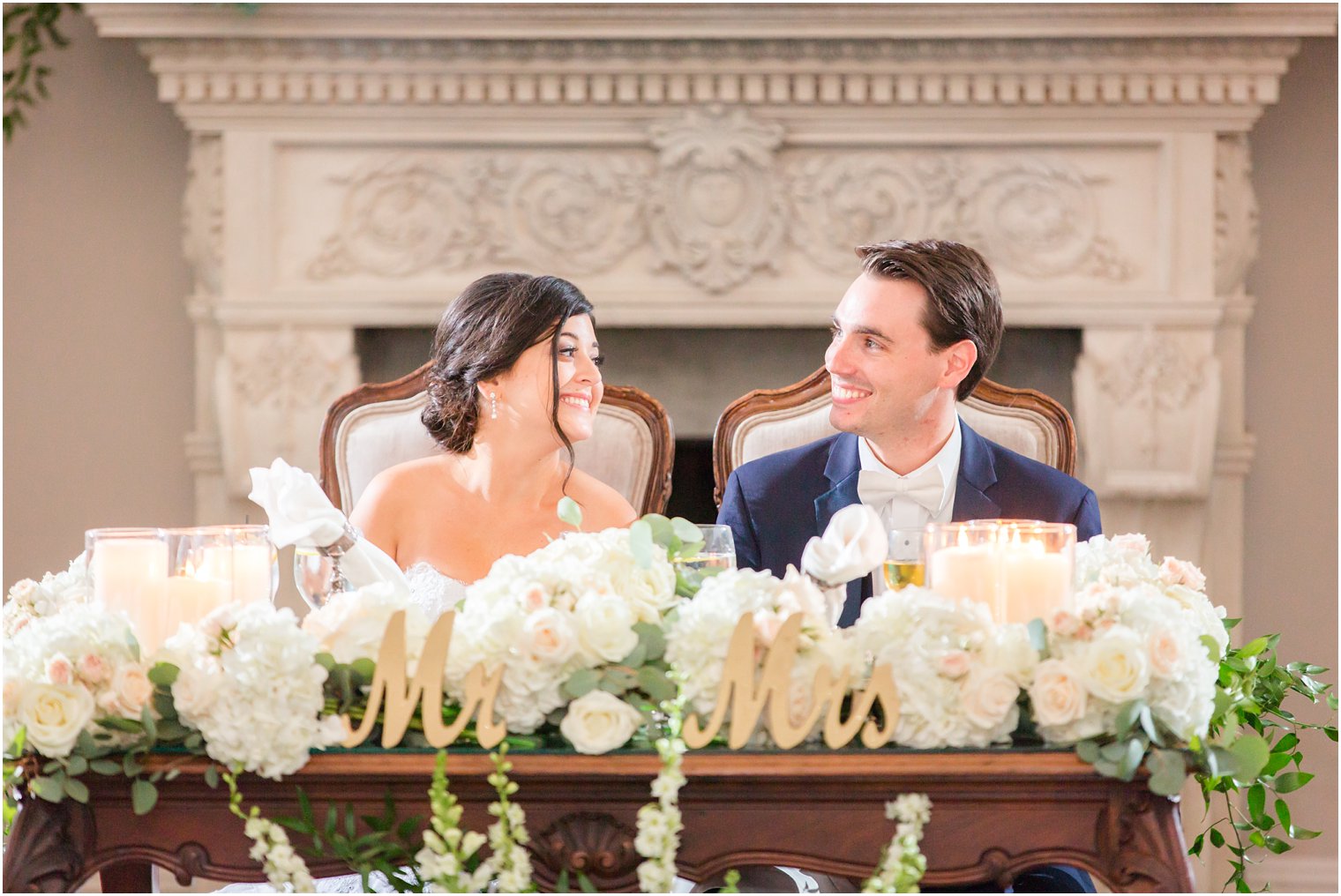 bride and groom grinning at sweetheart table with florals by Crest Florist photographed by Idalia Photography