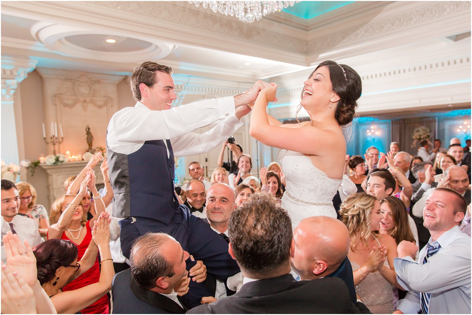 bride and groom hold hands while guests lift them up on dance floor at Park Savoy Estate 