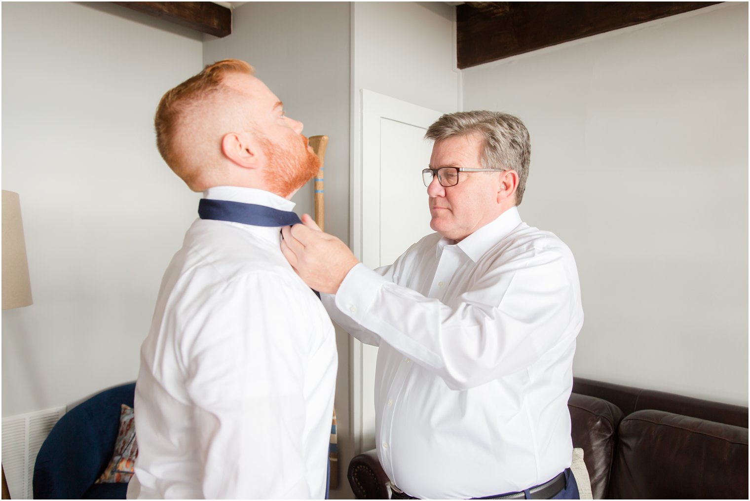 groom gets tie put on before wedding day photographed by Idalia Photography