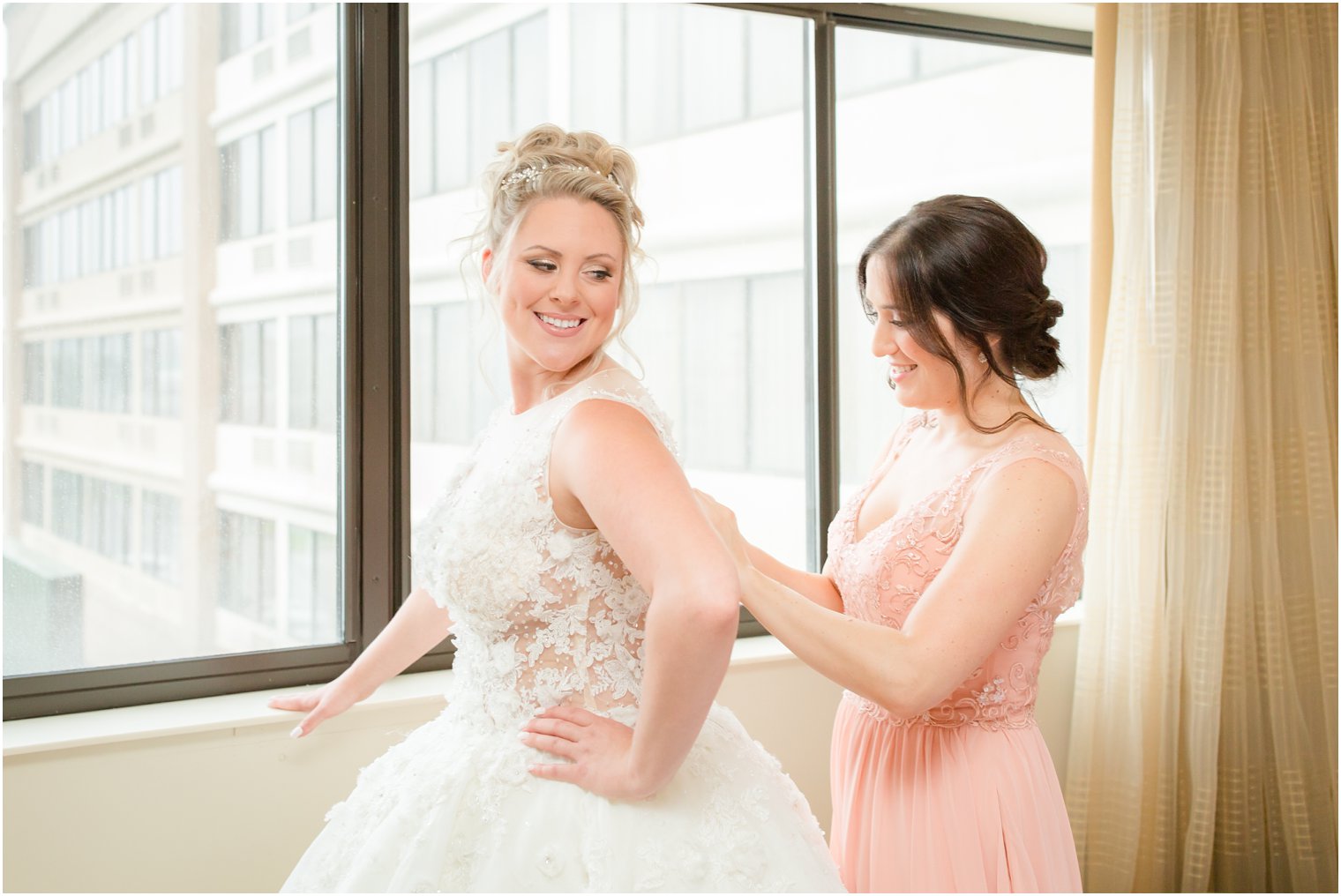 bridesmaid helps bride into her wedding gown before North Jersey wedding day photographed by Idalia Photography