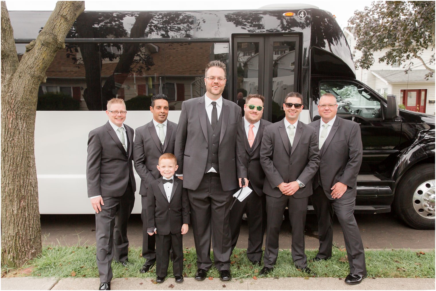 Groom and groomsmen wait to board Moonlight Limousine Service Inc.'s bus by Idalia Photography