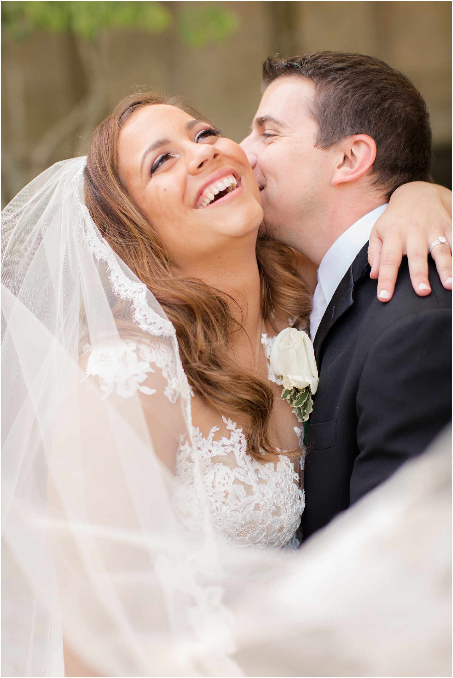 photo of bride laughing while groom kisses her