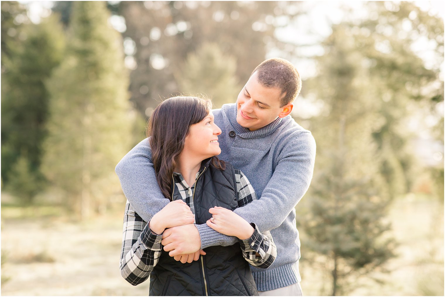 cute couple posing for photos for a winter Christmas tree farm engagement