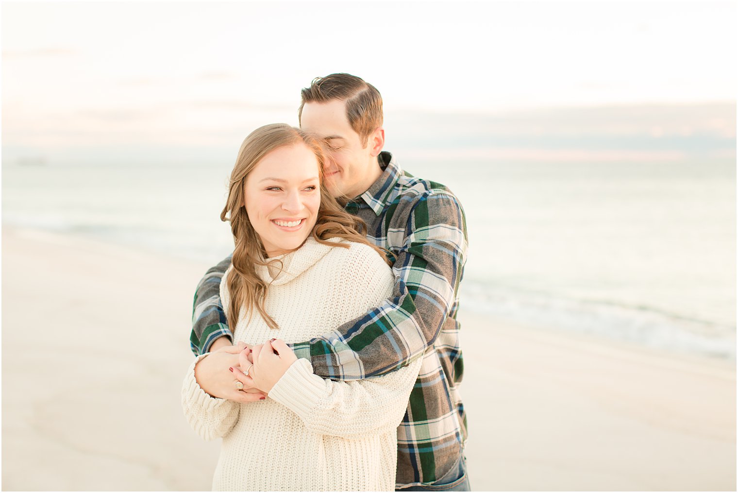 engaged couple cuddling on the beach at sunrise