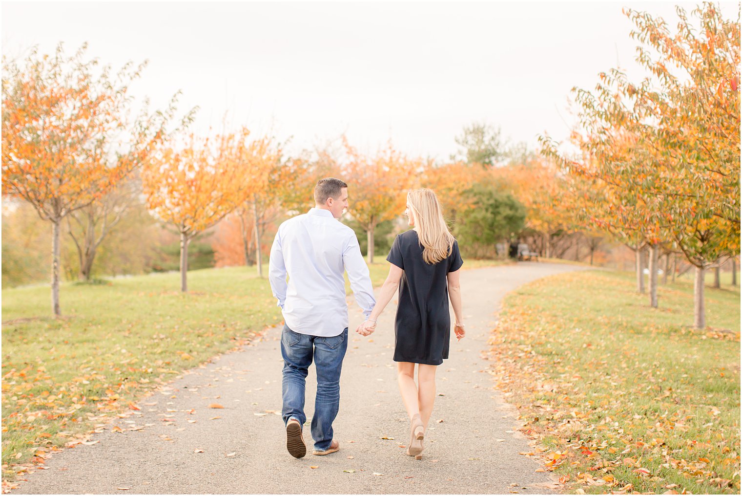 Couple walking during engagement session with fall foliage at Liberty State Park