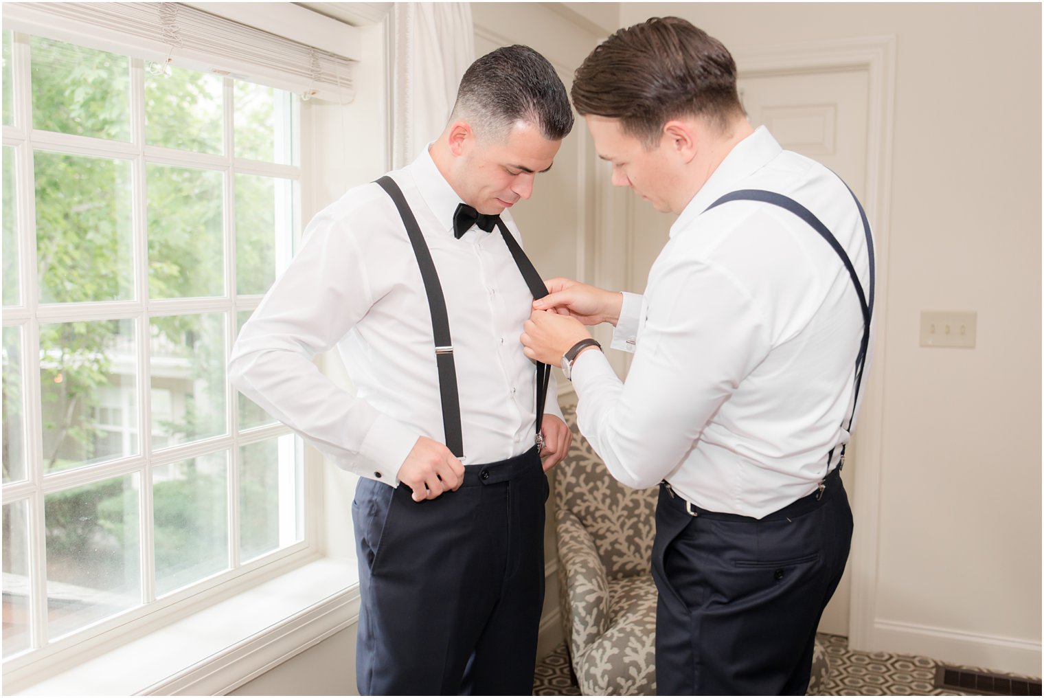 Groom putting on suspenders with best man