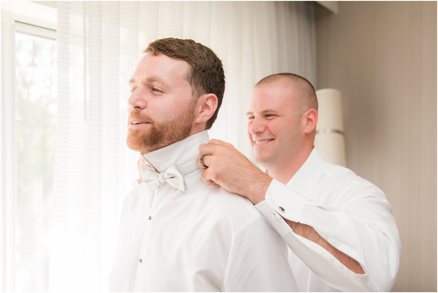 Best man helping groom put on bow tie