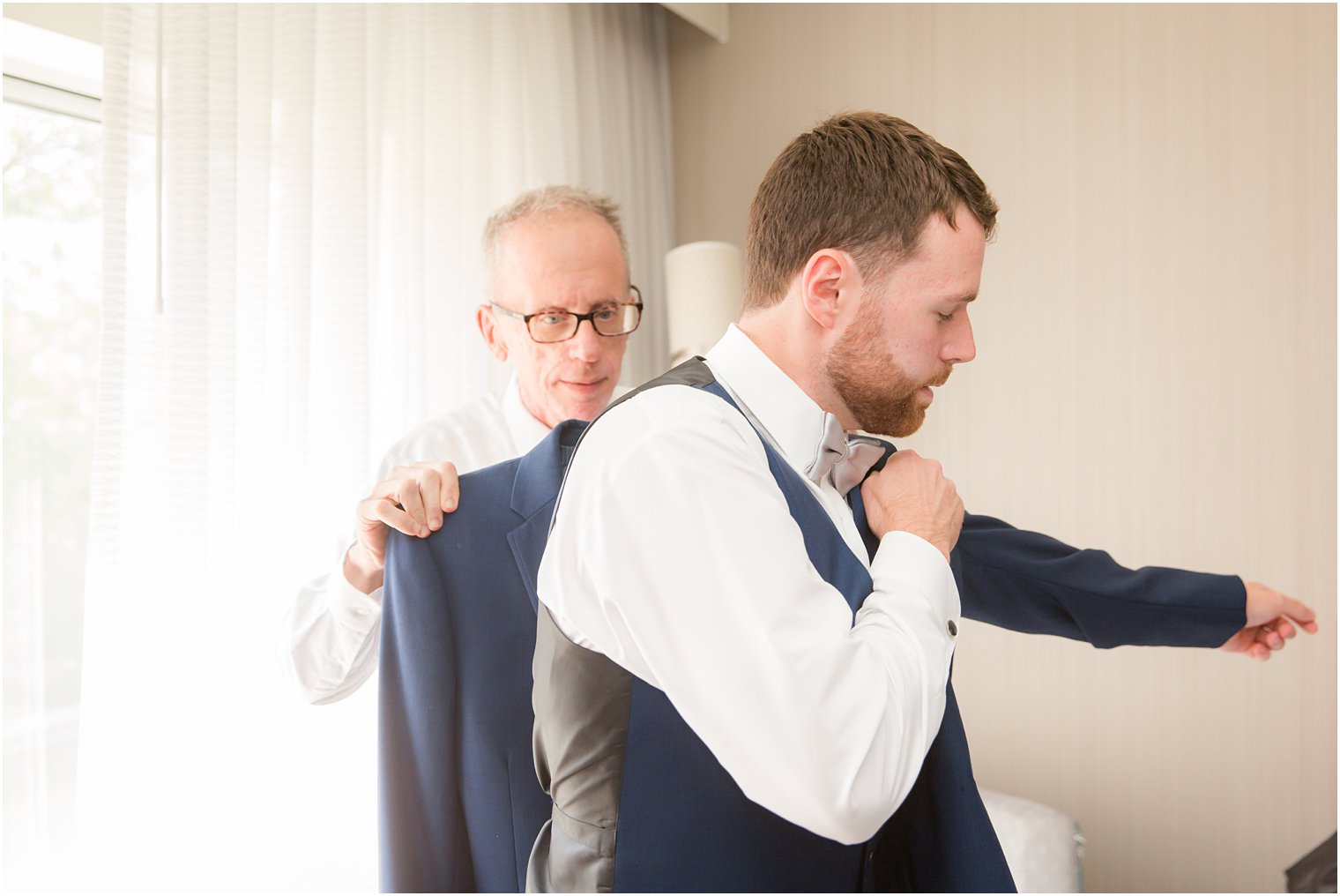 father helping groom put on his suit jacket