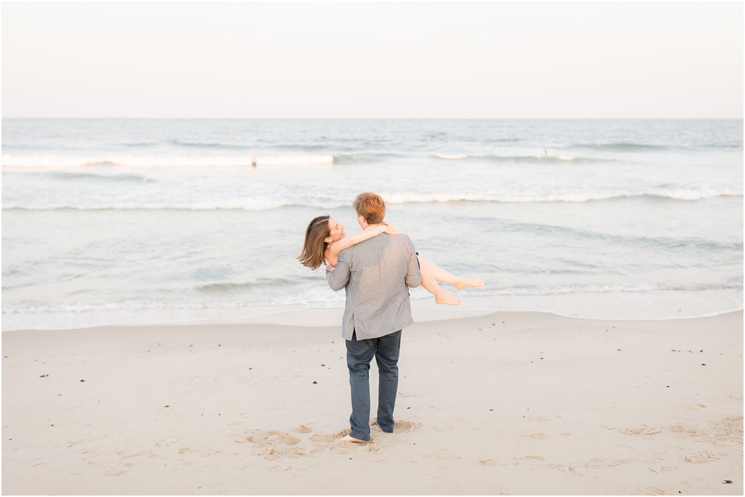 Groom lifting his bride in a romantic beach engagement session 