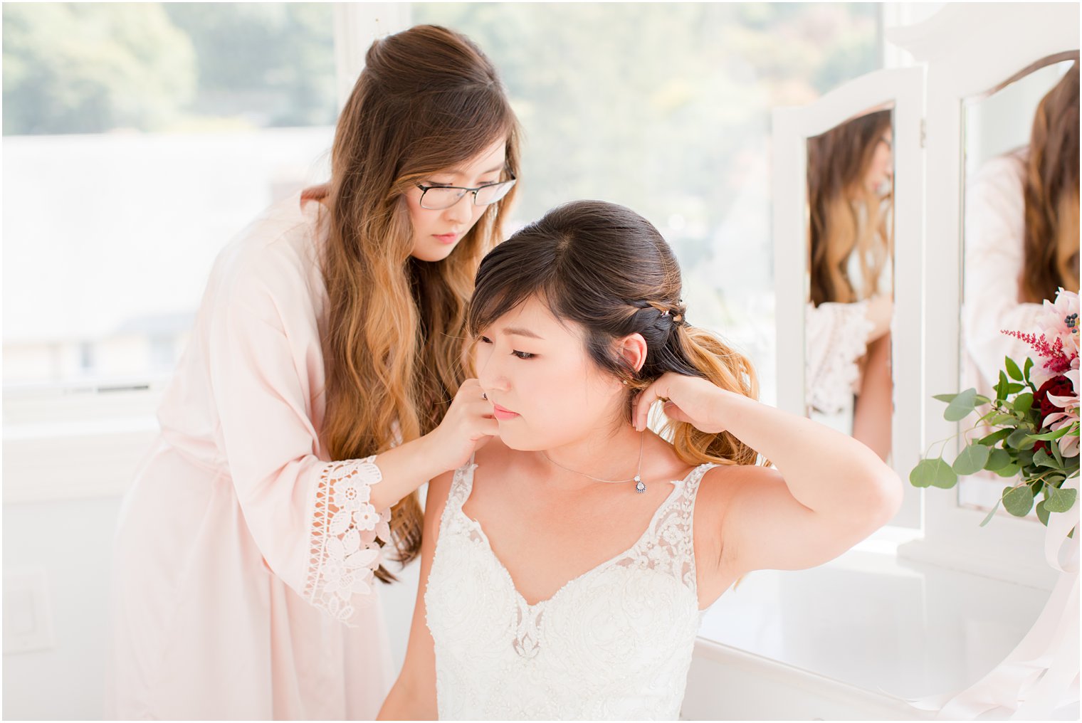 bridesmaid helps bride with jewelry on wedding day