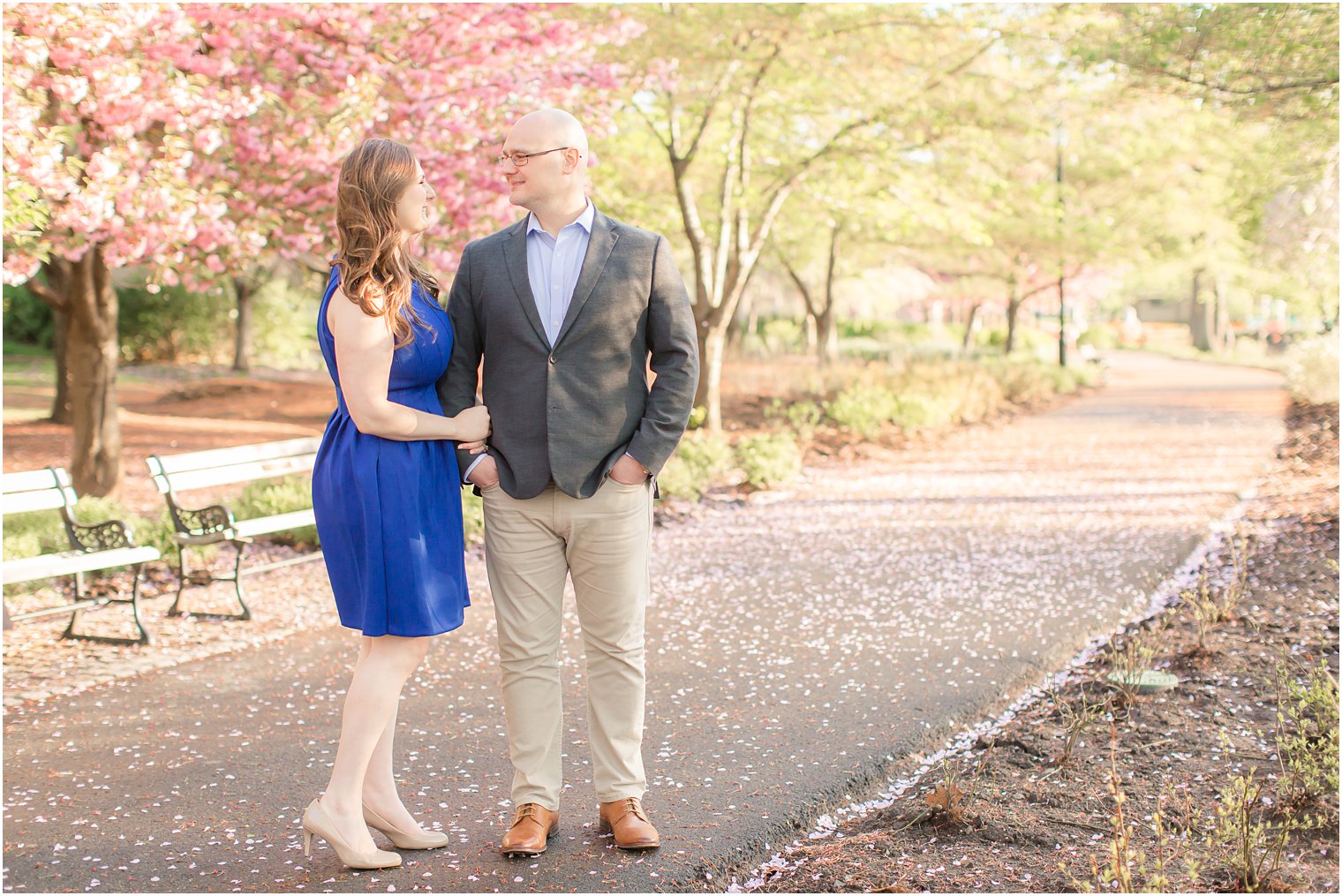 Engaged couple standing in a path among cherry blossoms at Branch Brook Park in Newark, NJ