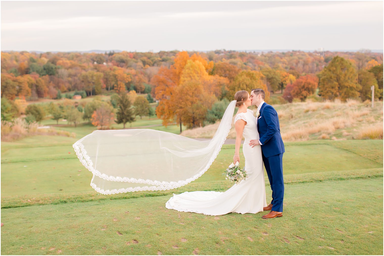 Bride and groom kissing in front of fall foliage at New York Country Club