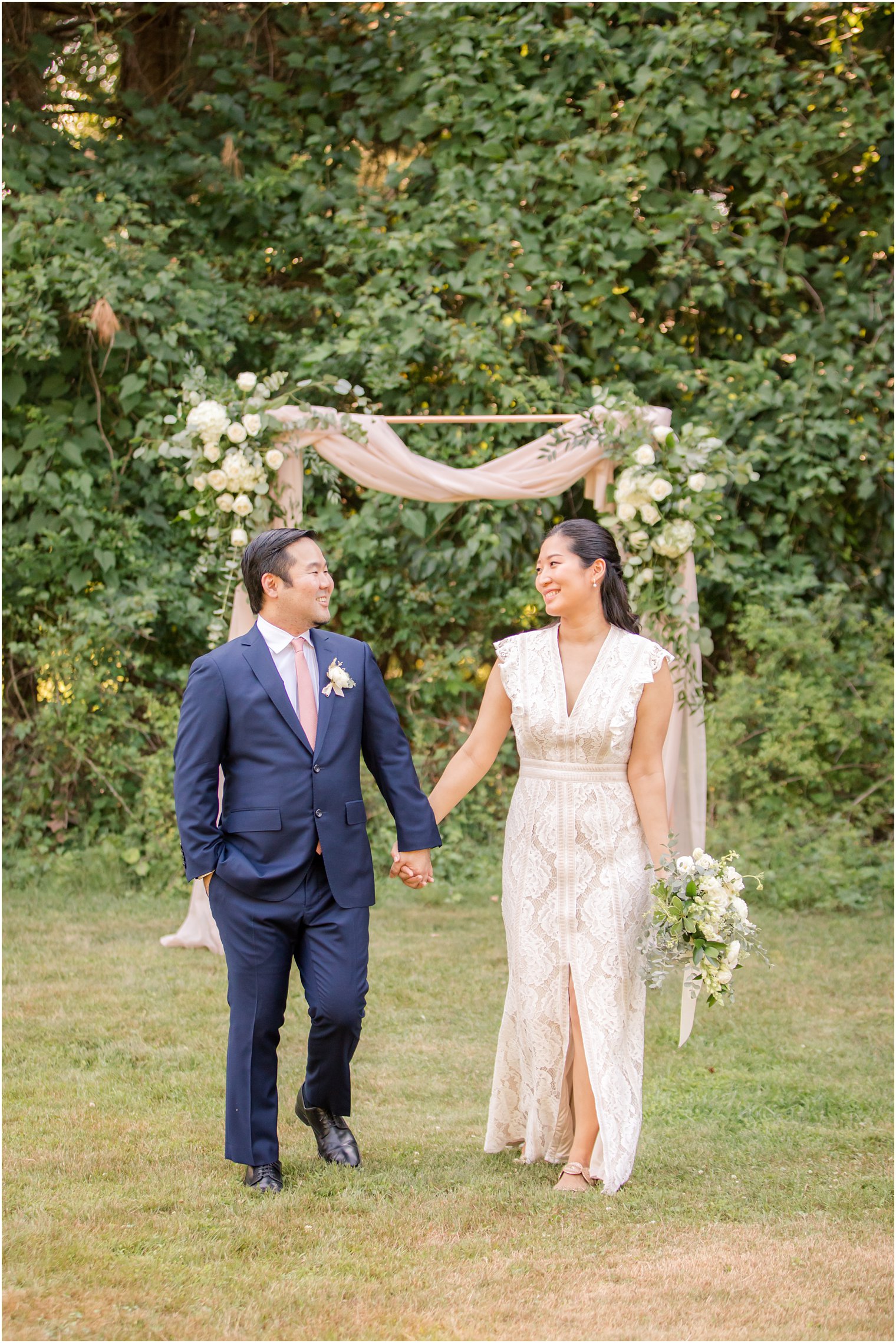 Bride and groom walking in front of a gorgeous floral arch