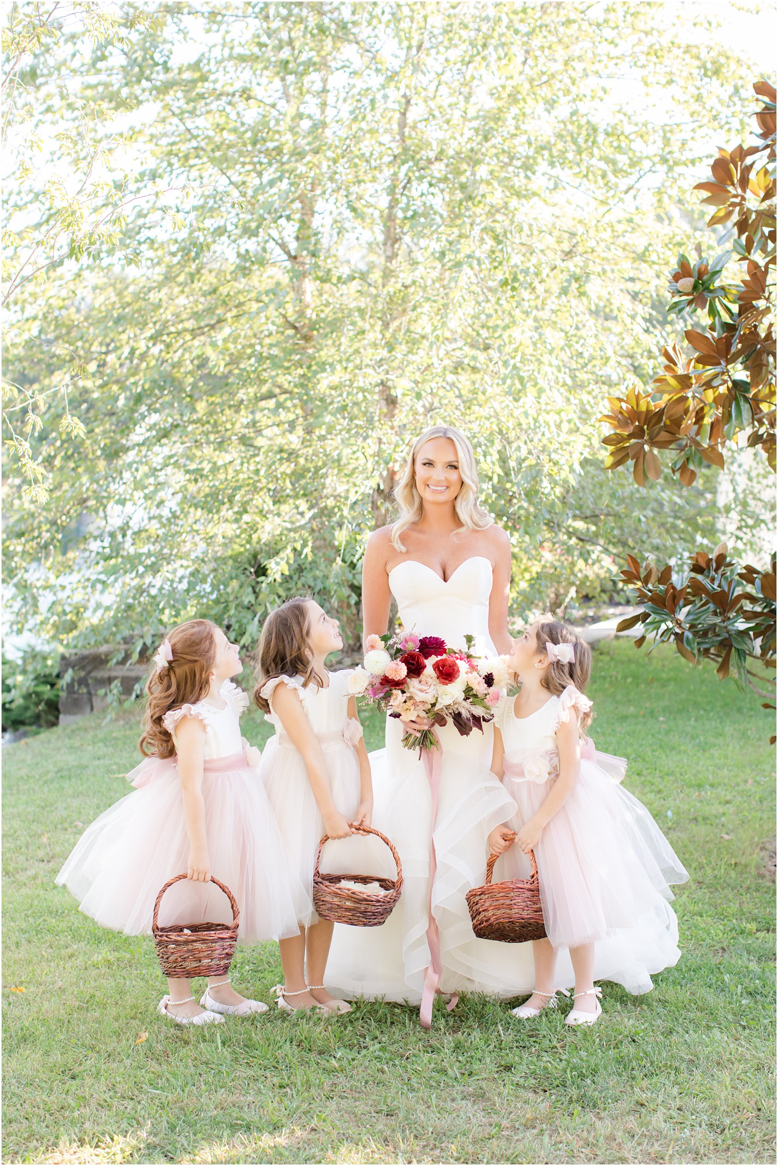 3 flower girls in pink dresses with baskets of flowers look up at bride 