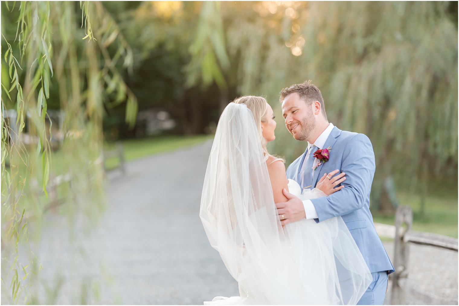 groom holds bride during portraits by willow tree