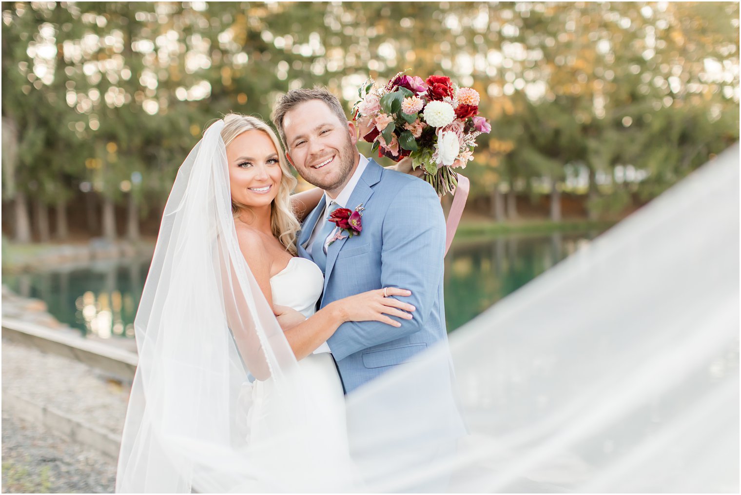 newlyweds lean heads together while veil floats around them at sunset