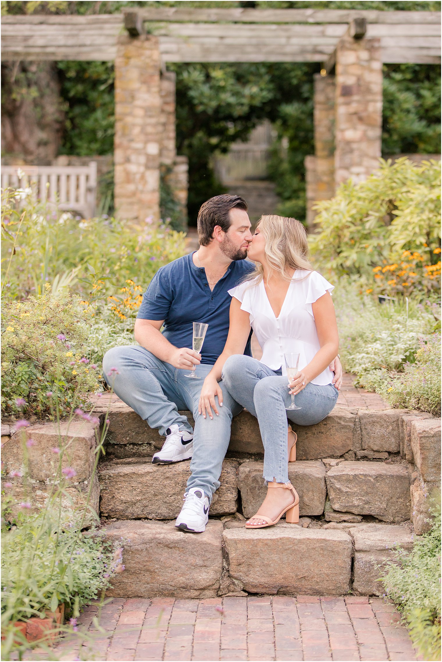 bride and groom sit on steps during Cross Estate Gardens engagement photos with champagne flutes