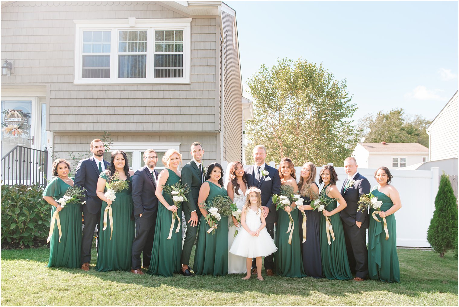 bridal party in emerald green gowns with black suits pose outside Tom's River home