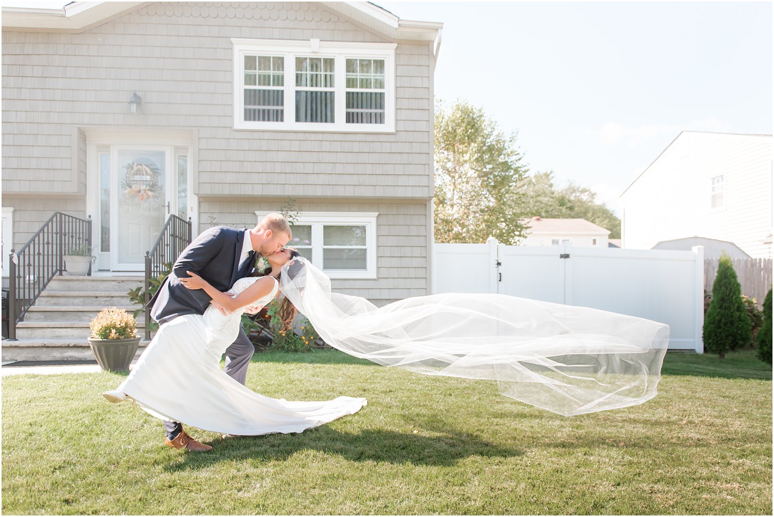 groom kisses bride while dipping her and veil floating in air