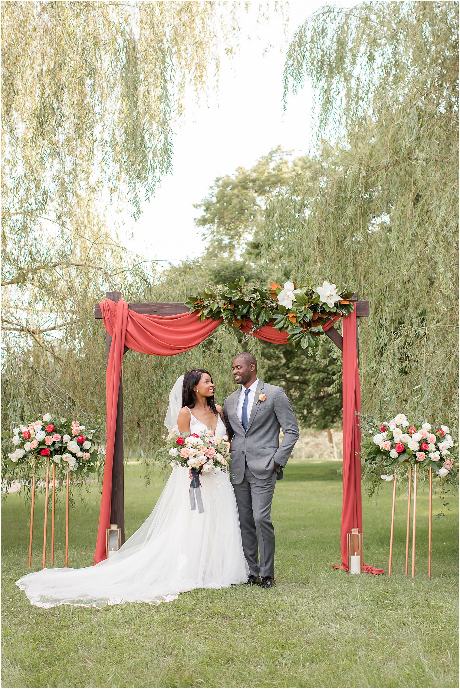 bride and groom pose under arbor with florals and red fabric drop for fall wedding