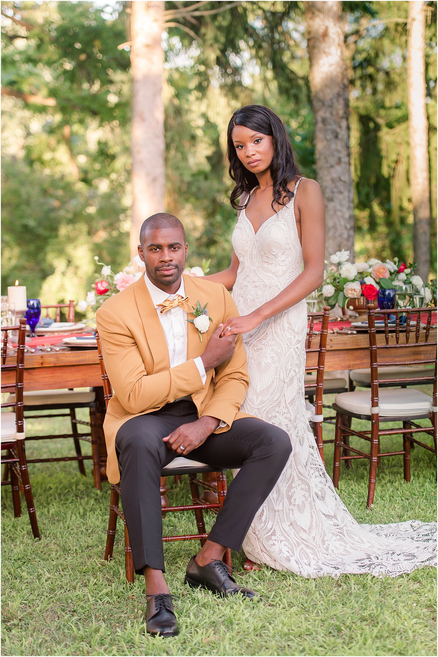 groom in mustard suit jacket holds bride's hand in front of reception tablescape