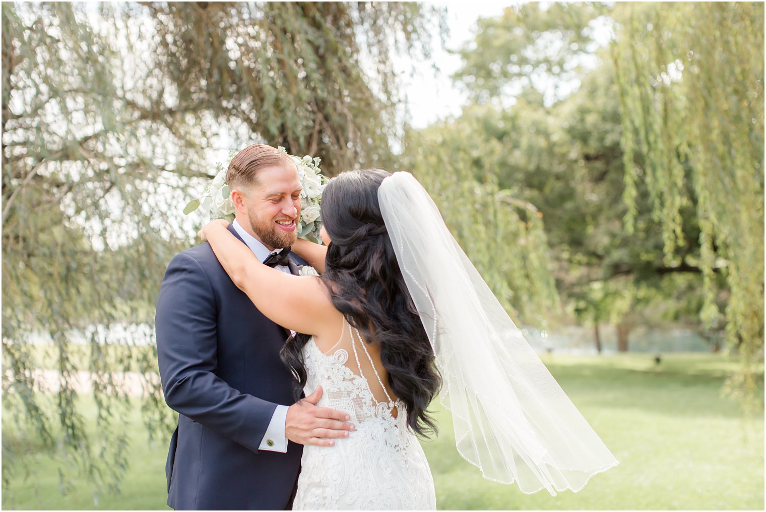 bride holds onto groom's neck with veil blowing in the wind