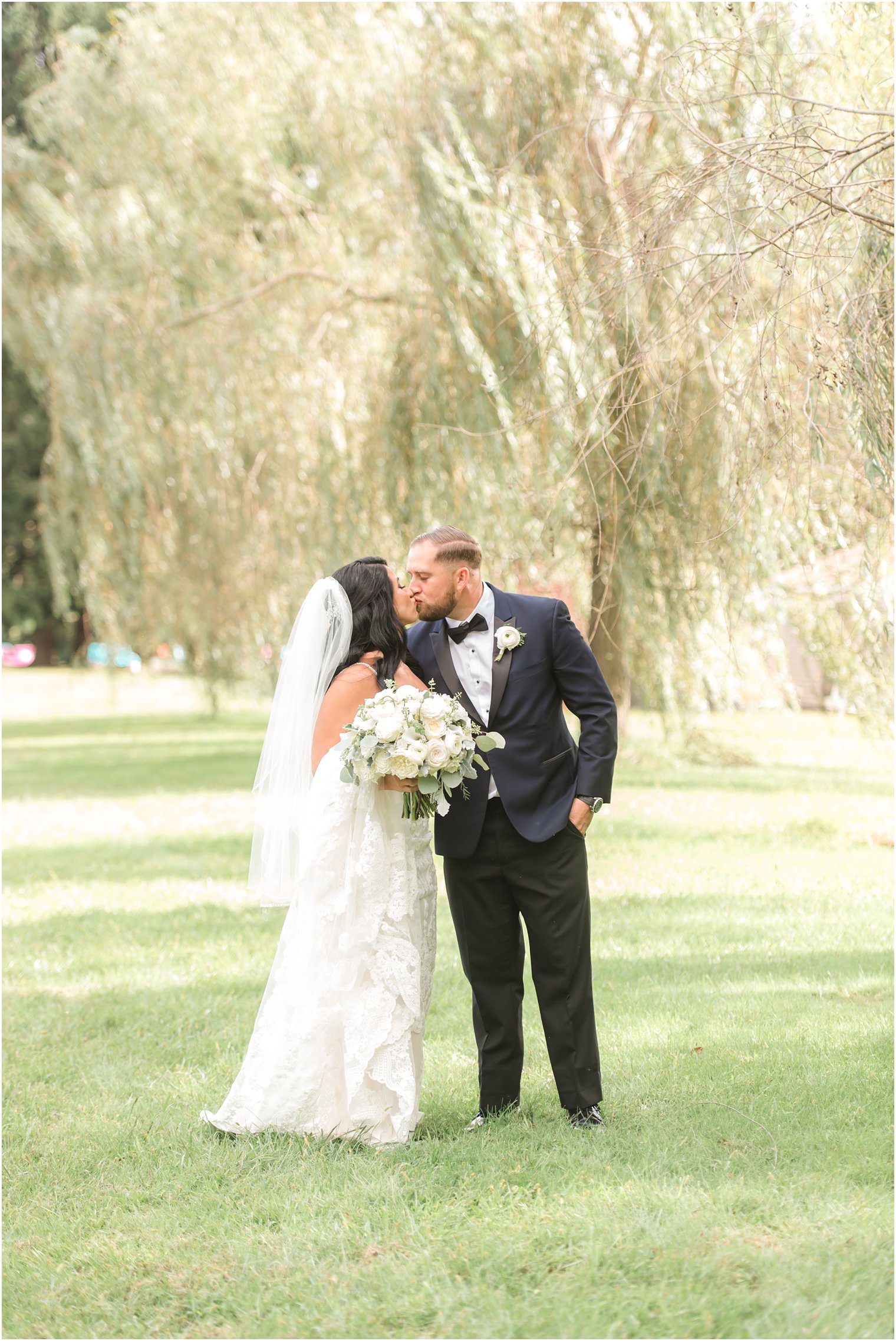 bride and groom kiss by willow tree before rustic modern wedding at Windows on the Water at Frogbridge