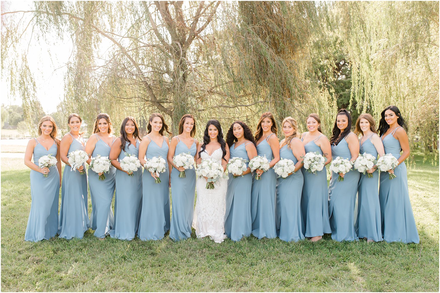 bridesmaids in dusty blue gowns hold all-white flowers at Windows on the Water at Frogbridge