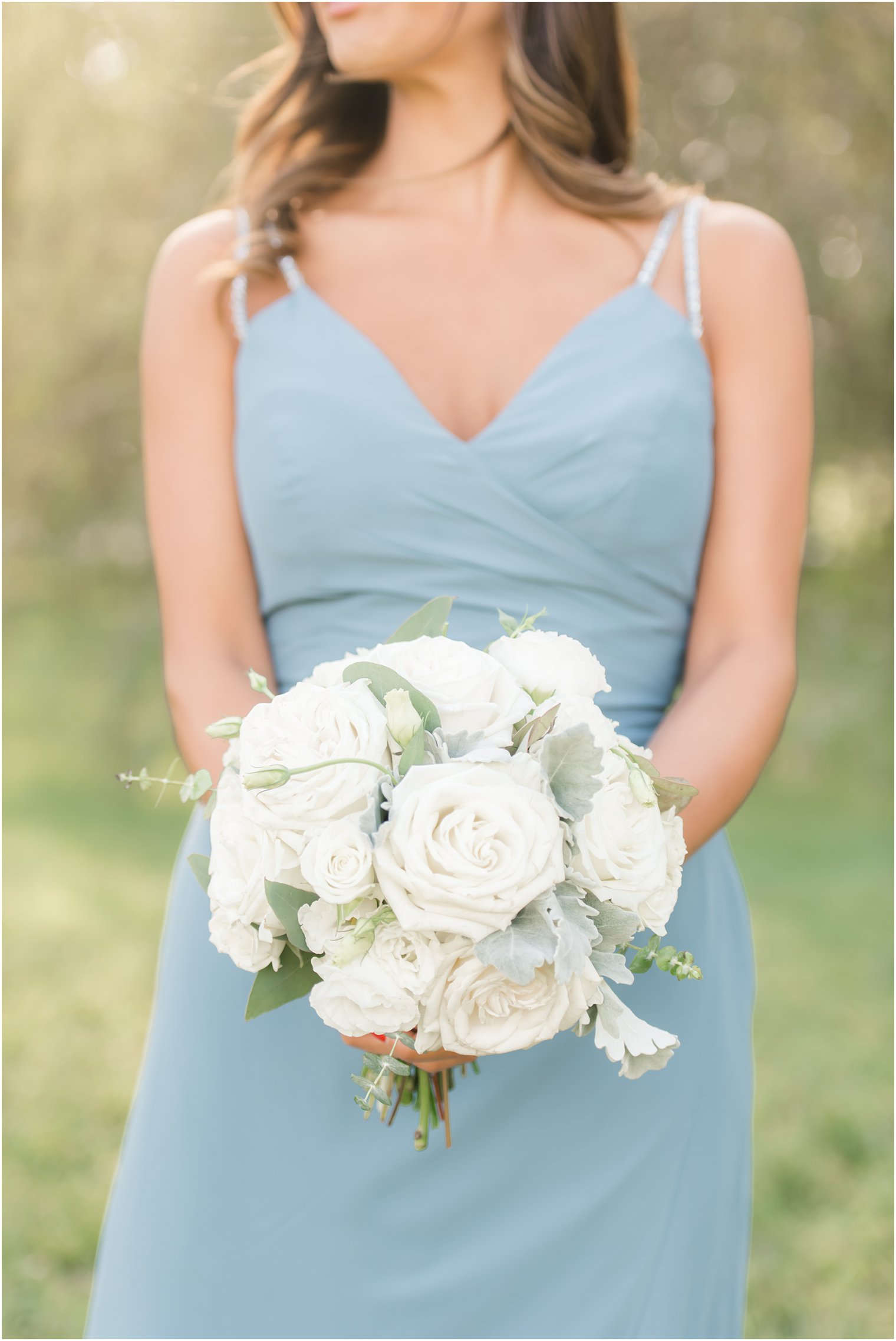 bride in dusty blue dress holds bouquet of all-white roses