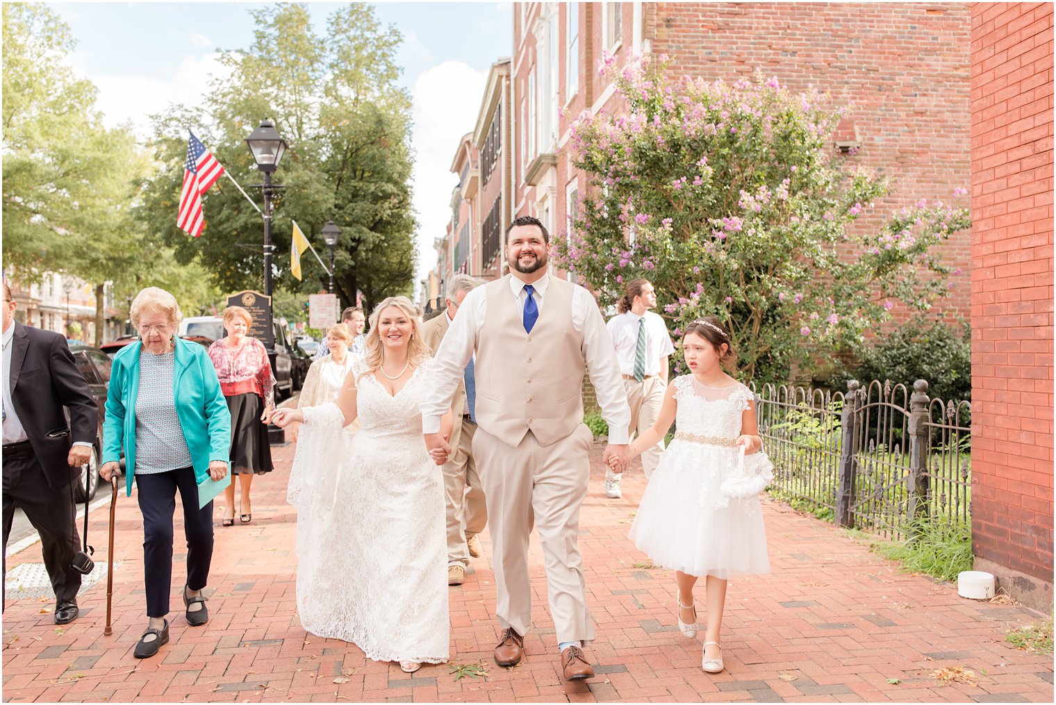 groom walks down street in Burlington NJ with bride and daughter