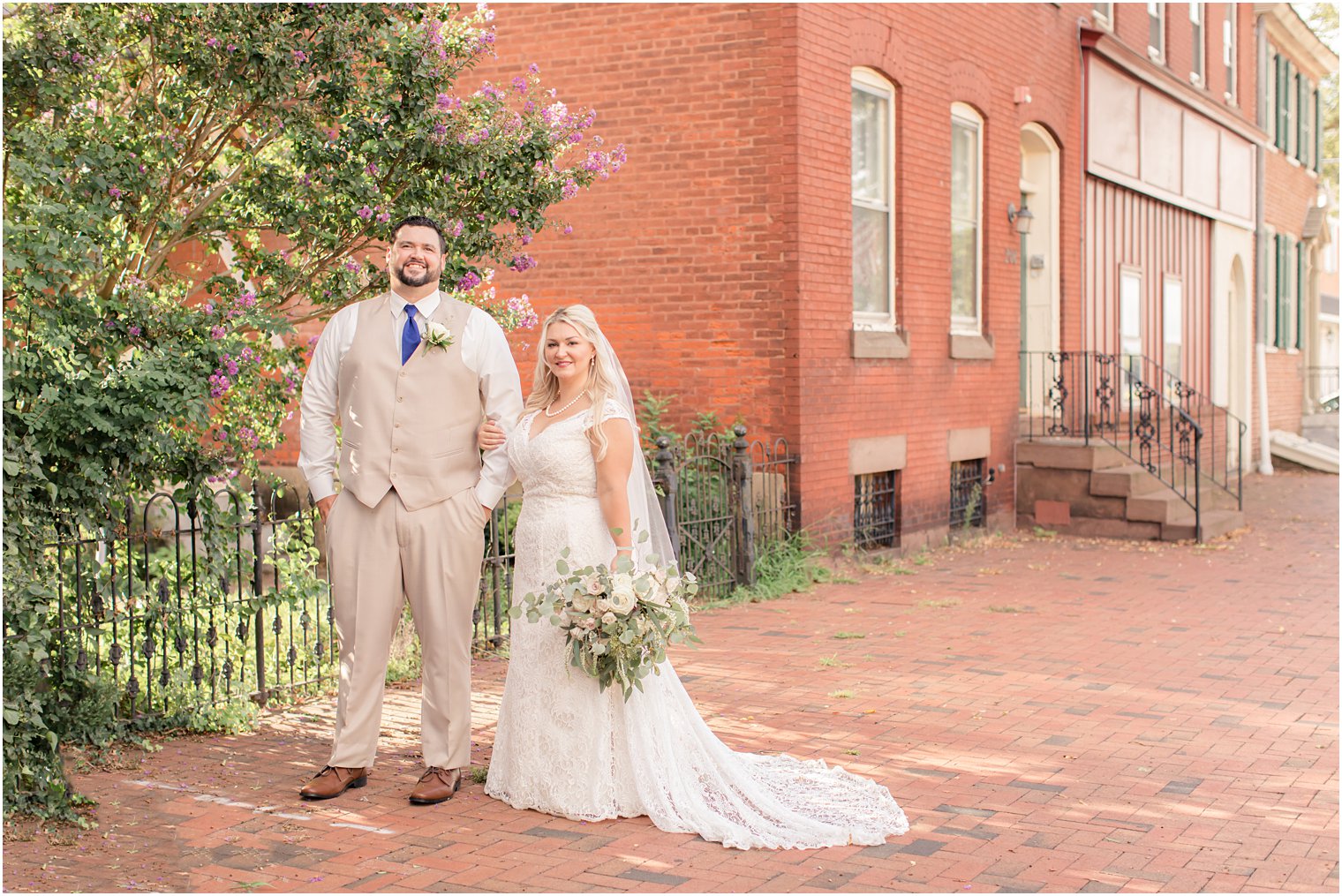 newlyweds pose by purple flowering tree and The Lily Inn