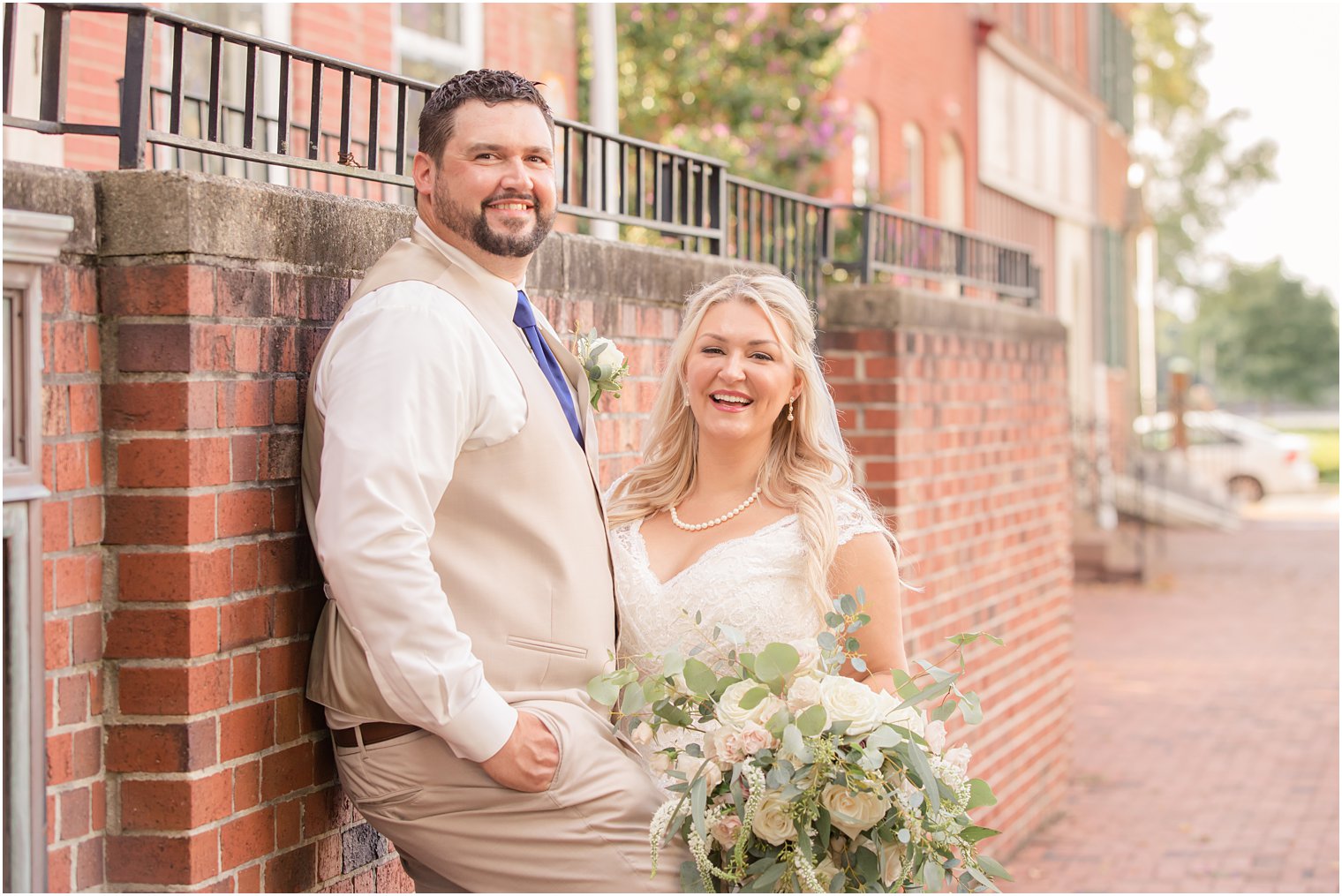 bride and groom laugh during wedding portraits on the street of Burlington NJ