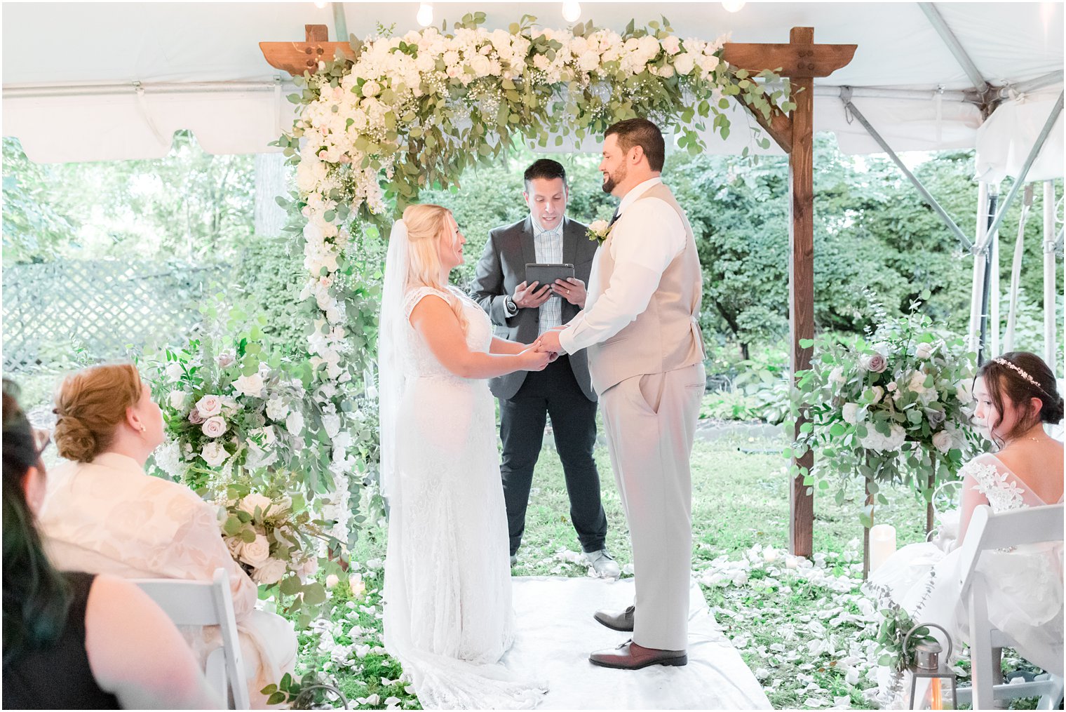 newlyweds exchange vows under wooden arbor with white flowers