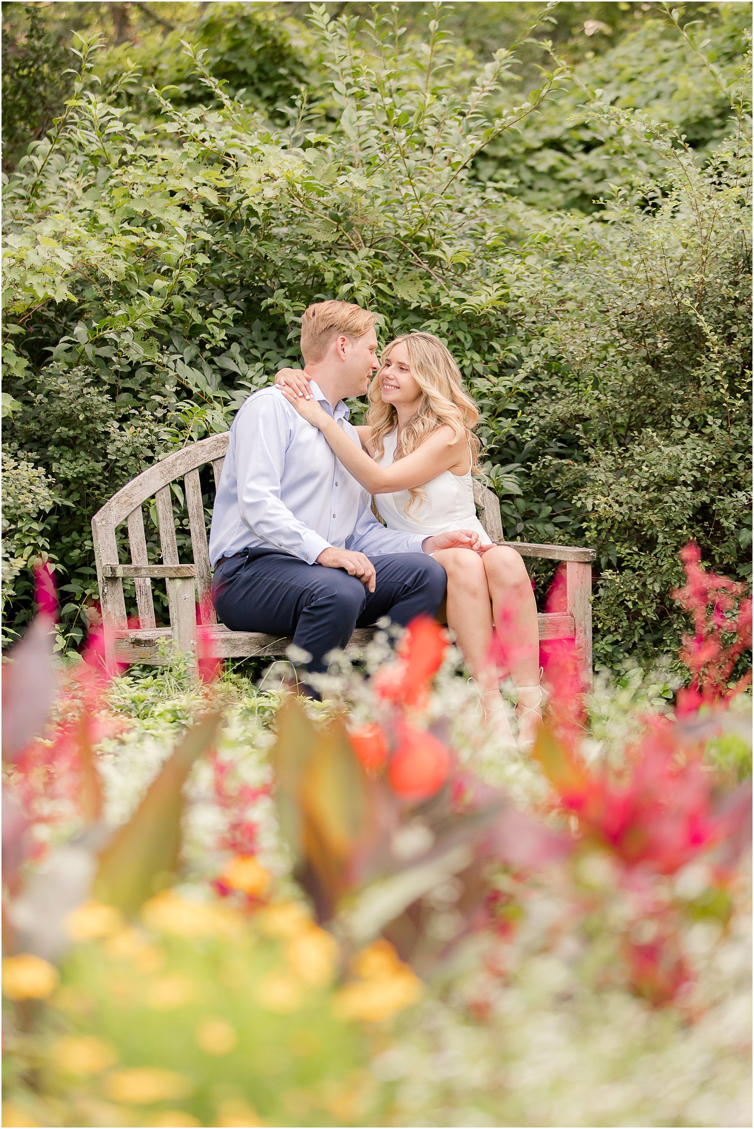 couple poses on bench during Skylands Manor Engagement Session in the summer