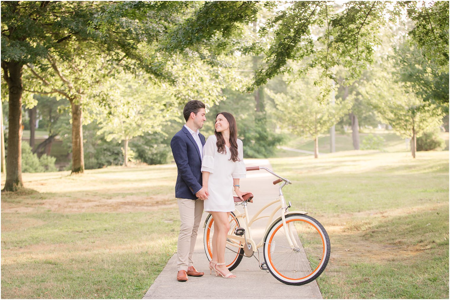 bride in white dress poses with groom in navy jacket by bike