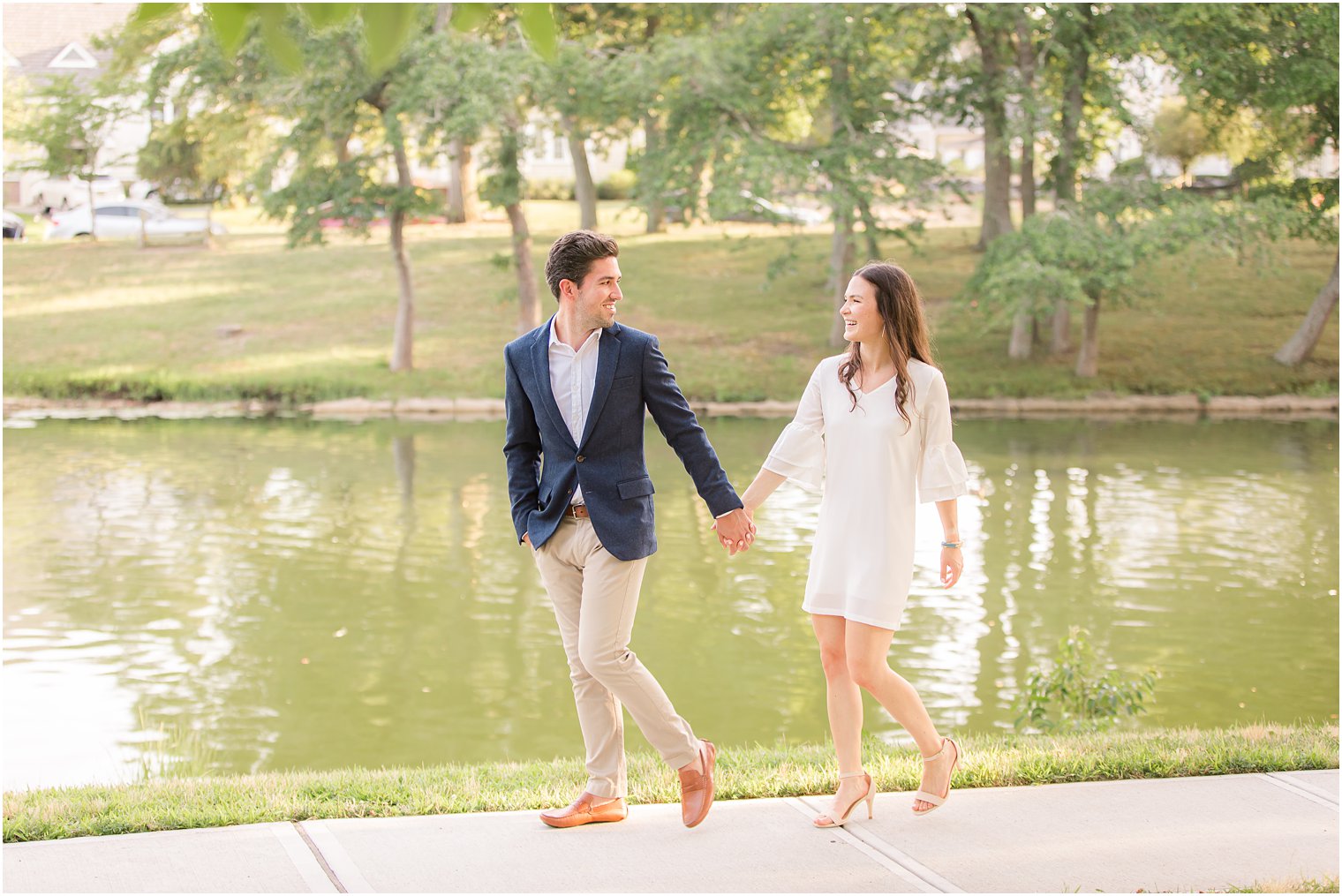 bride and groom hold hands while walking by lake