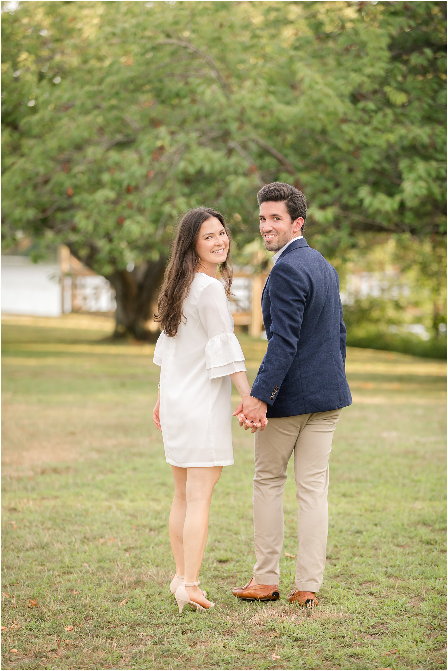 engaged couple holds hands while looking back at NJ wedding photographer