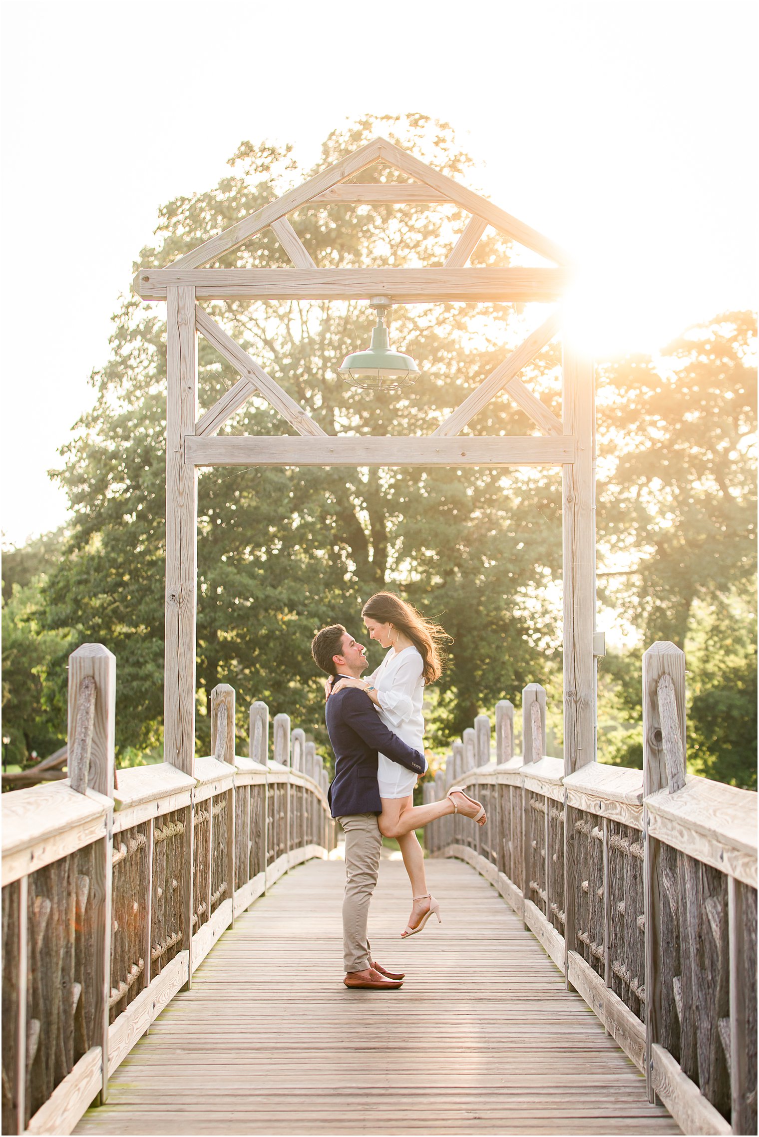 groom lifts bride while standing on wooden bridge in New Jersey