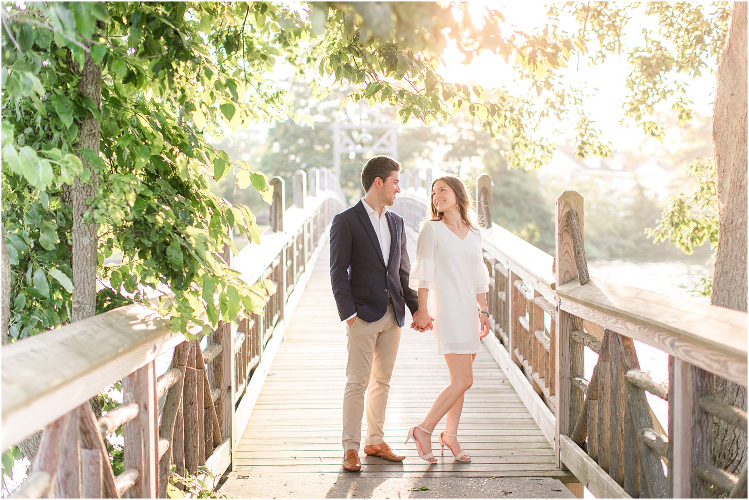 bride and groom hold hands standing on bridge in Spring Lake at sunset